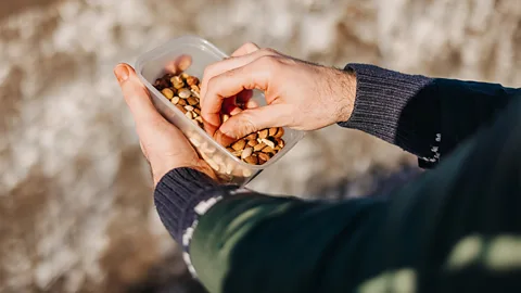 A man picking mixed nuts out of a plastic box (Credit: Getty Images)