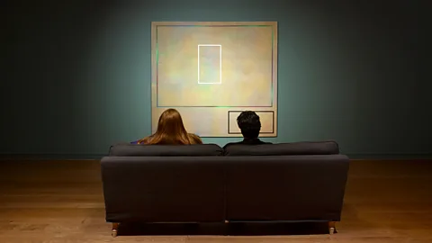 Two people photographed from behind, sat on a sofa infront of an abstract painting, in the Room to Breathe installation at Manchester Art Gallery (Credit Manchester Art Gallery/ Michael Pollard)