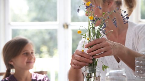 A mum and daughters putting flowers in a glass jar full of water