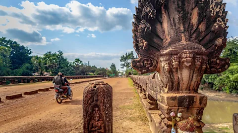 Alamy Motorcycle drives past a stone statue lined road in Cambodia (Credit: Alamy)