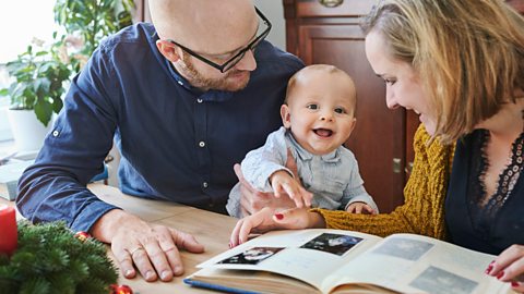 Father, mother and baby looking at pictures in an album together.