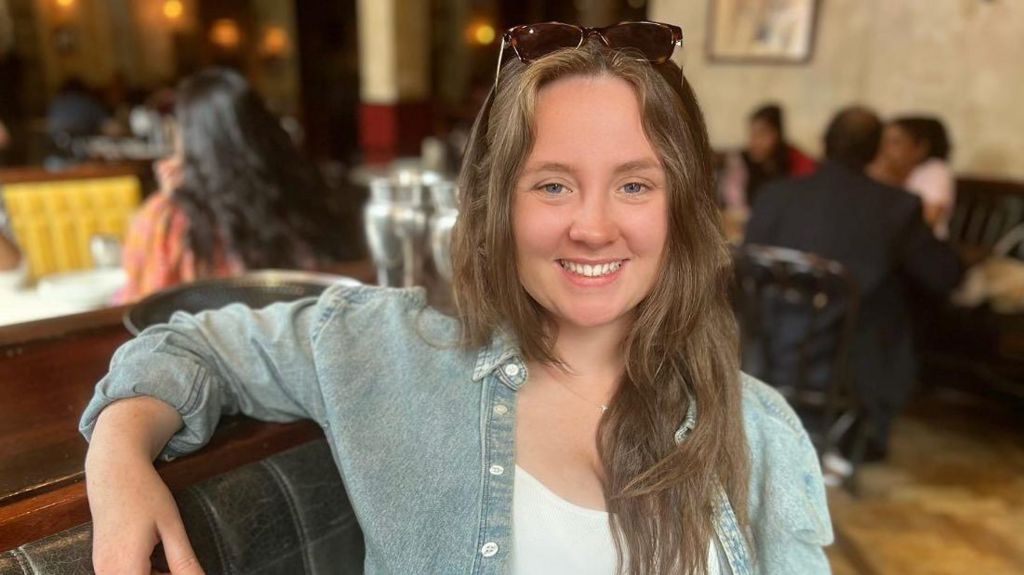 Trainee solicitor Niamh sitting in a restaurant smiling at the camera, with sunglasses on her head