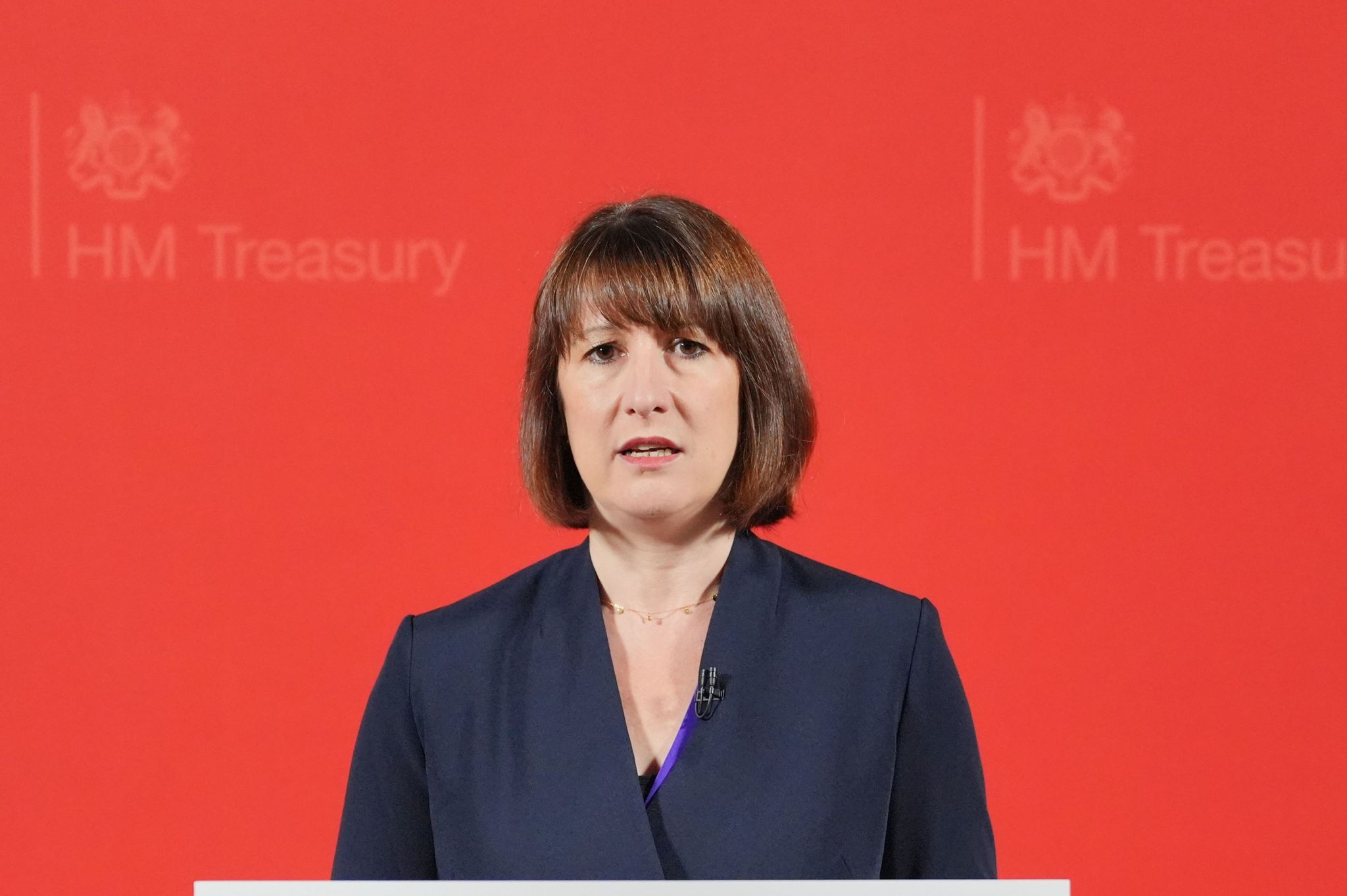 Rachel Reeves standing in front of a red background with the words HM Treasury emblazoned on