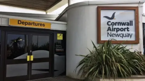 Entrance door to the departures zone of Newquay Airport. A yellow sign with black letters says departures above a set of double doors. There is also a sign saying Cornwall Airport Newquay visible.