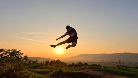 A man jumping and silhouetted against the sun in the background