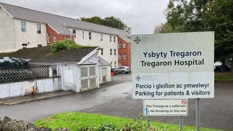 Sign saying Ysbyty Tregaron or Tregaron Hospital to the right with the hospital building to the left.