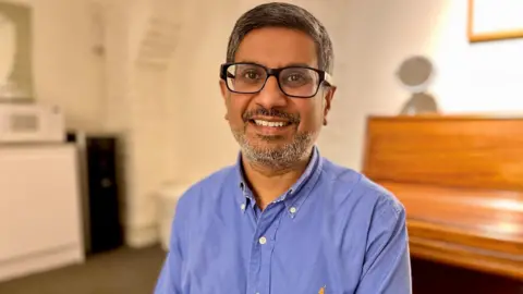 Samir wearing glasses and a blue shirt smiling at the camera