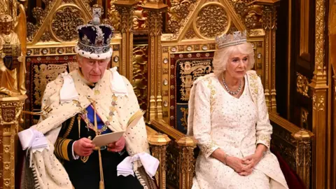 Leon Neal/PA Media King Charles III delivers a speech beside Queen Camilla during the State Opening of Parliament in the House of Lords at the Palace of Westminster in London