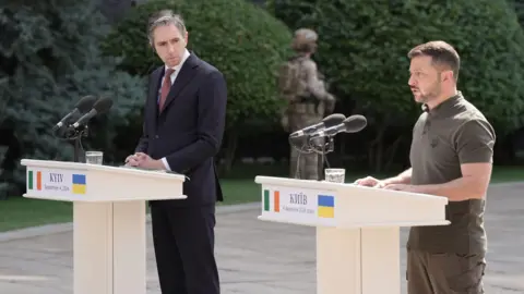 PA Media Simon Harris and Volodymyr Zelensky speaking at podiums outside