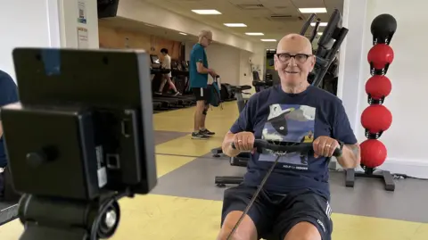 Eric Ayling smiling whilst working out on a rower