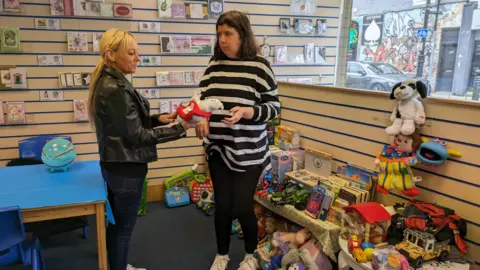 NEAS Two adult woman looking at a stuffed toy in a room filled with toys and books.