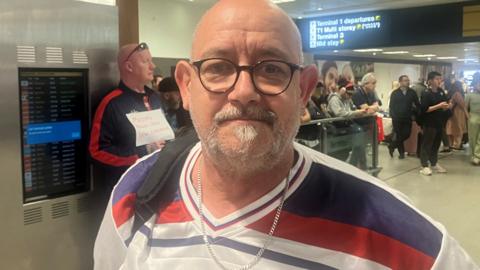 Andrew McCloud in legacy England shirt at arrivals in Manchester Airport