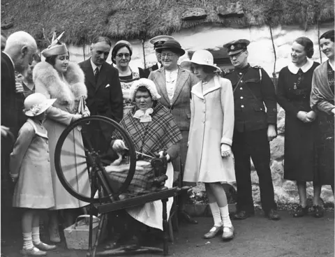 Getty Images Queen Elizabeth, Queen Consort to King George VI (left) with Princesses Elizabeth (right) and Margaret Rose, watching a spinner at work in a Scottish Highland village.