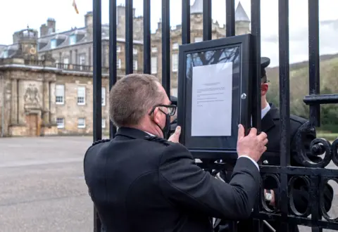 AFP A member of staff attaches a notice to the gates of the Palace of Holyrood house in Edinburgh