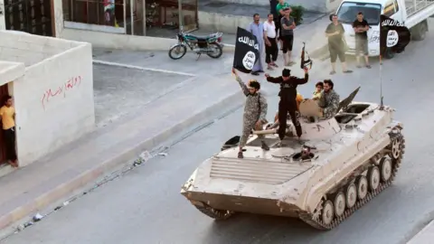 Reuters IS militants hold up black jihadist banners in Raqqa on 30 June 2014