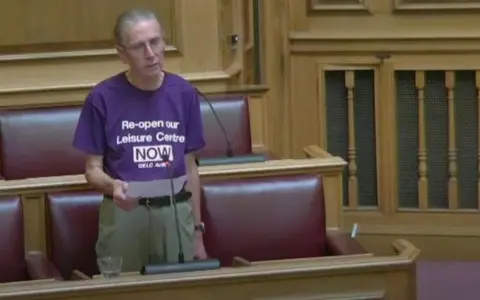 Dorset Council Steve Parlour addressing the council meeting and wearing a purple t-shirt bearing the slogan: Re-open our leisure centre now