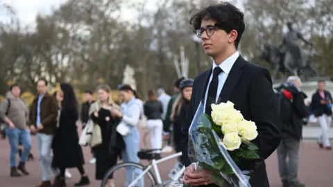 EPA A man holds a bouquet of flowers outside Buckingham Palace on 9 April 2021