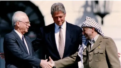 Reuters Yitzhak Rabin and Yasser Arafat shake hands as US President Bill Clinton looks on - 1993 picture