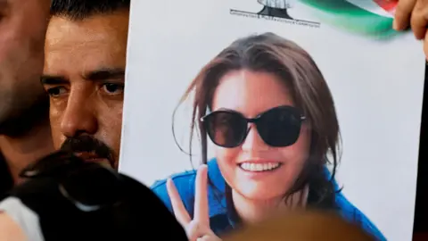 Reuters  Photo of Aysenur Ezgi Eygi wearing sunglasses and blue shirt on a poster held by man with a mustache