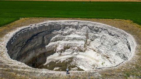 aerial photograph shows farmer Yigit Aksel walking around a giant sinkhole formed in the middle of the fields in Karapinar in the central Anatolian province of Konya, on June 23, 2024. 