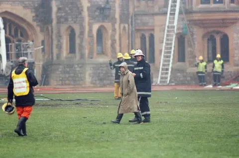 Getty Images The Queen is escorted by the chief fire officer around the grounds of Windsor Castle as fire fighters battle a fire, 20 November 1992.