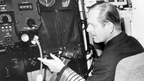 PA Media The Duke of Edinburgh, in uniform of the Admiral of the Fleet, sits at the wheel of the nuclear-powered submarine HMS Churchill