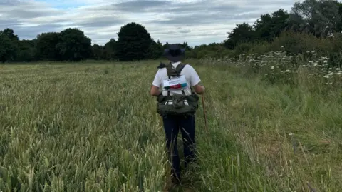 Philip Burlingham Philip with his back to the camera walking through a field of grass with a walking stick