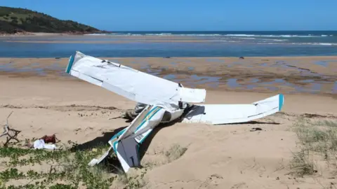 A light plane which has crashed on sand with the ocean in the background