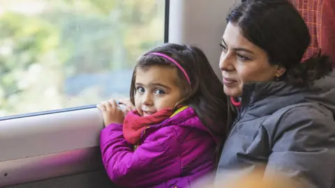 Mother and daughter wearing winter coats and looking out the window of a train