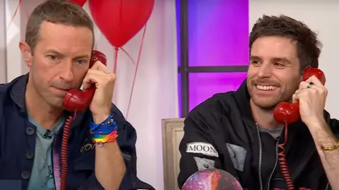 Chris Martin and Guy Berryman of Coldplay take phone calls from fans during an appearance on the shopping channel QVC