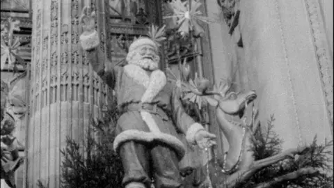 A black and white image of a Father Christmas decoration stood on a sleigh