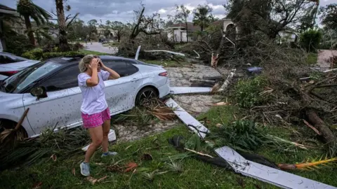 A woman holds her head while assessing damage from Storm Milton