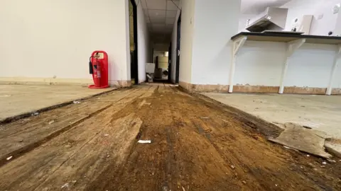 A wooden floor which has been damaged after flooding. Some areas of the floor still appear to be wet.