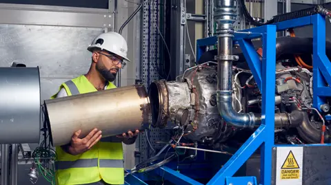 Ihab Amed working on the test jet engine. He's connecting a metal tube to another piece of equipment.