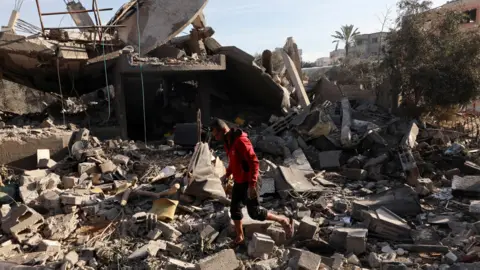 A Palestinian man walks over rubble following an Israeli air strike on a home in Nuseirat refugee camp, central Gaza (11 December 2024)