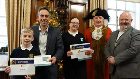 Hull City Council Oscar and Lilah at Hull Guildhall in their school uniforms holding their winners' certificates standing alongside the Lord Mayor in red robes and black feathered hat, leader Mike Ross and the council's chief executive  Matt Jukes who are wearing dark suits