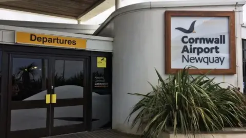 Entrance door to the departures zone of Newquay Airport. A yellow sign with black letters says departures above a set of double doors. There is also a sign saying Cornwall Airport Newquay visible.