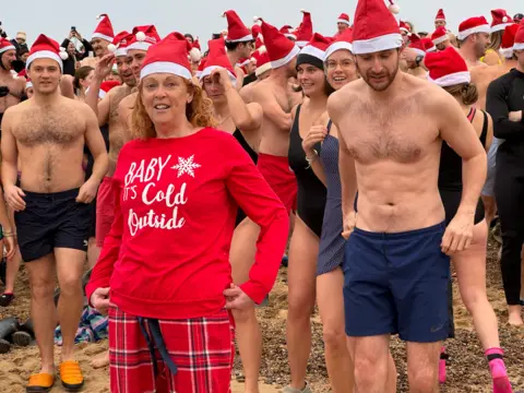 Runners dressed in Santa hats line up on the beach ready to run into the sea.