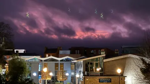 Mr BU A dark purple sky over several buildings. One has a sign on that says 'Waterside Centre'. Within the sky there is also shades of pink.