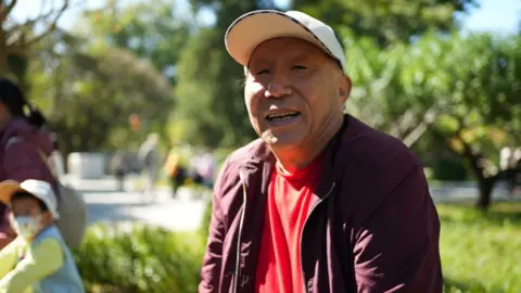 Mr Meng, sat in Ritan Park wearing a white cap and mauve jacket