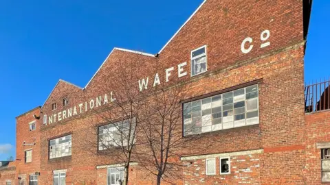 LDRS Progress Works, Ayres Road, Old Trafford, a red brick building with a tree in the foreground on a sunny day with the words 'international wafe co' emblazoned on the front of the building, 