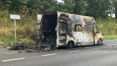 Newton Abbot Fire Station A burnt-out ambulance. The white paint is visible but all the markings have been burnt away, along with the tyres. There is what looks like ash in the rear of the ambulance and all over the road. 