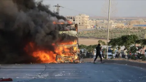 Truck burning, partially obscured by thick plume of black smoke