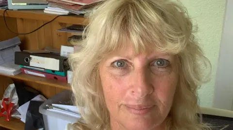 Anglia Research Services Eileen Lavelle, with pale blue/grey eyes and light blonde hair, sits in her office, surrounded by folders and boxes of notes.