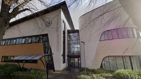 Google Entrance to Cheltenham East Fire Station with bushes and trees outside.