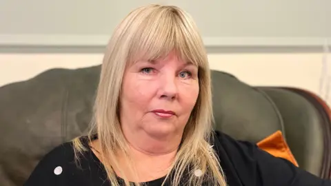 Stella McLoughlin - a woman with blonde hair sits in a grey sofa looking at the camera.