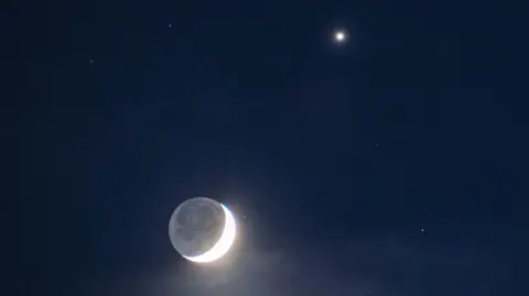 A crescent moon and Venus against a dark sky.