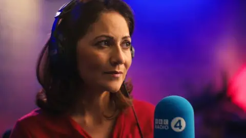 Mishal Husain wears headphones in a BBC Radio 4 studio in front of a microphone and bathed in soft lighting