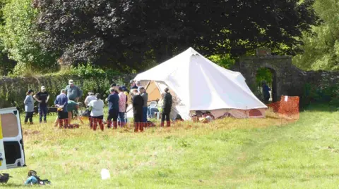 Cerne Historical Society A group of people standing in a field next to a large white bell tent.