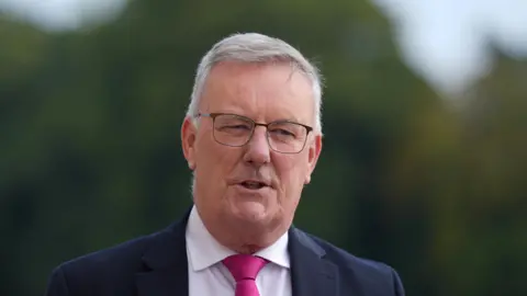 PA Media Mike Nesbitt wearing a dark coloured suit and a pink tie, with a white shirt. 